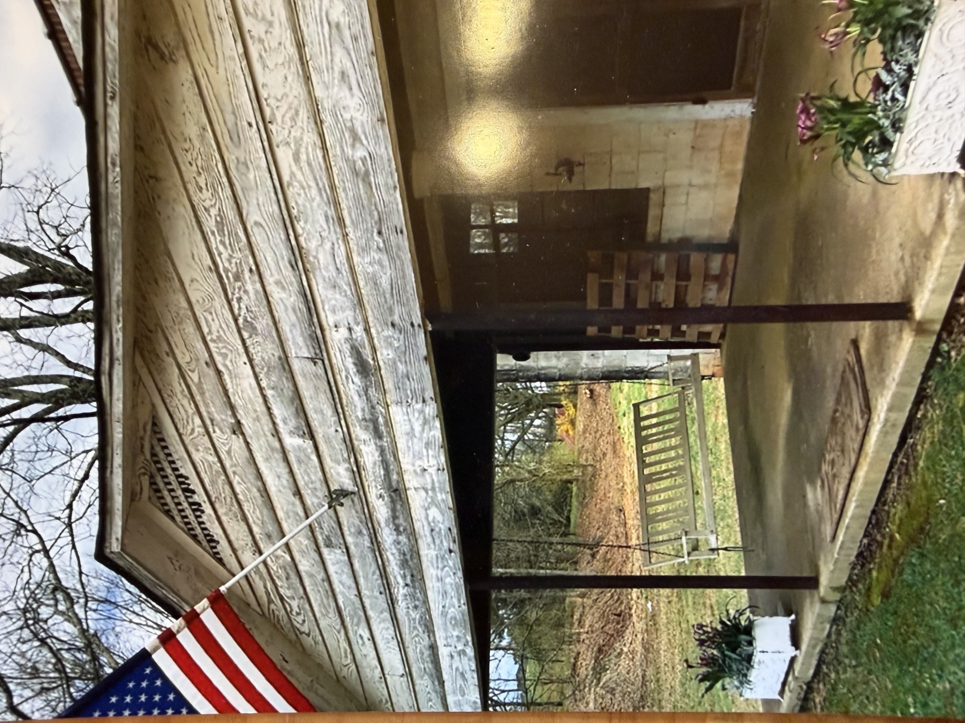 The front porch before restoration — weathered wood, American flag still flying, porch swing waiting